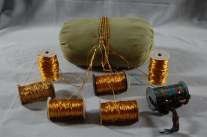 A cylindrical braid cushion stuffed with rice or lentils. The braid is made from six golden metallic threads (zari) and one strand of rainbow metallic strip thread (beginning of the 20th century, Oman.