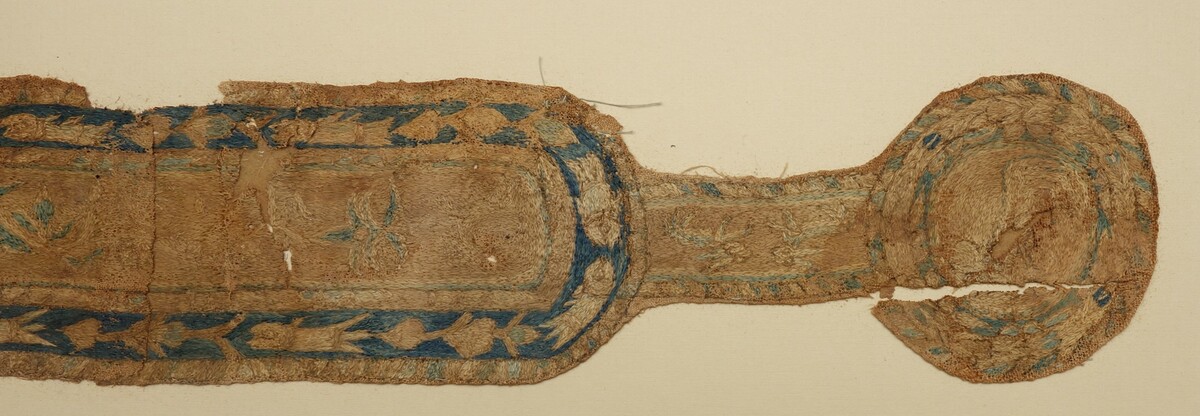 Fragment of a Coptic textile with an embroidered design of a clavus and a pendant, probably from a child's tunic. 6th-8th c. (TRC 2011.0460).