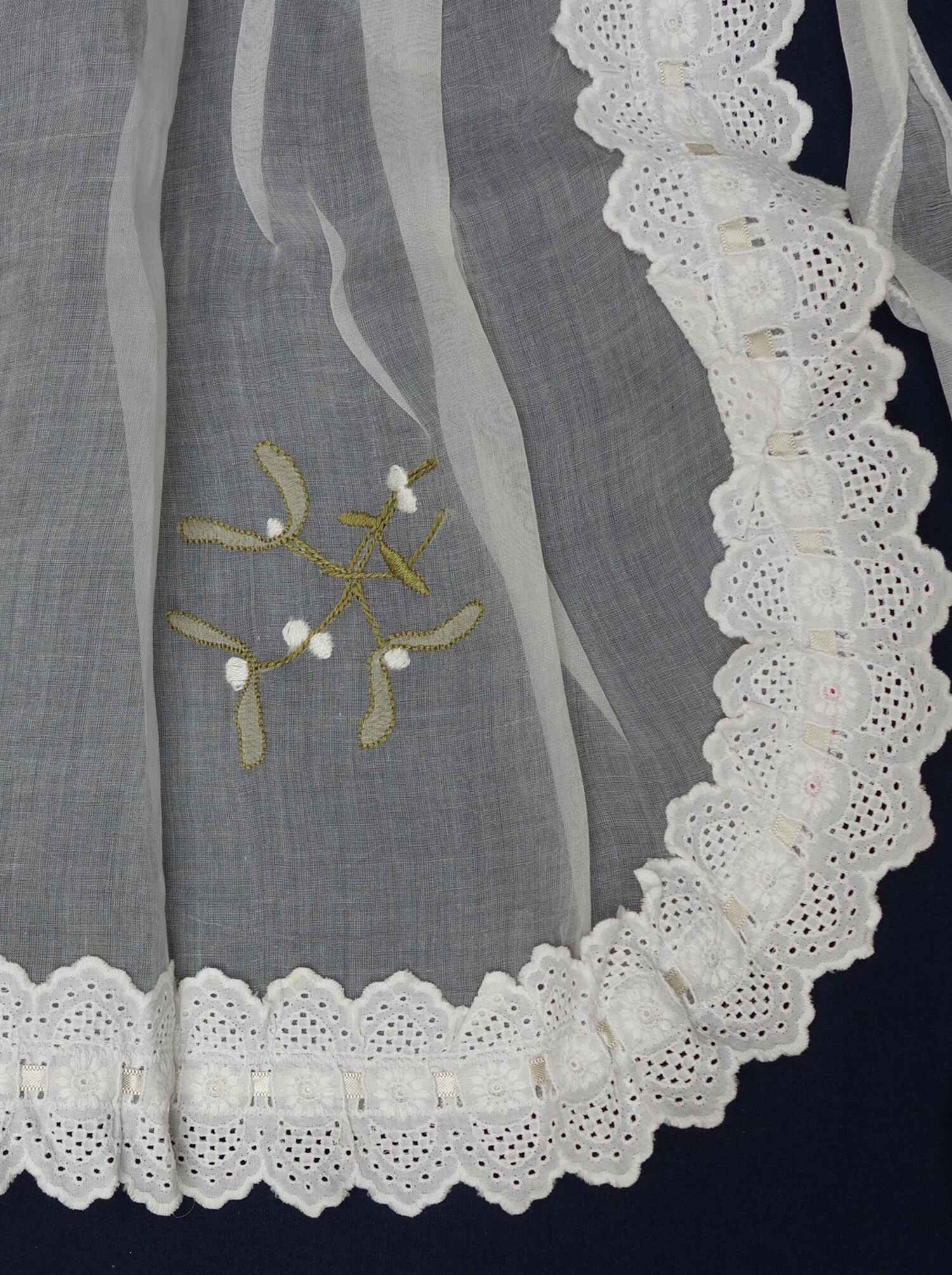 Detail of an apron with the leaves of the mistletoe worked in shadow work with herringbone stitch and the berries worked in satin stitch on the front of the cloth, Australia,1930s (TRC 2018.0303).