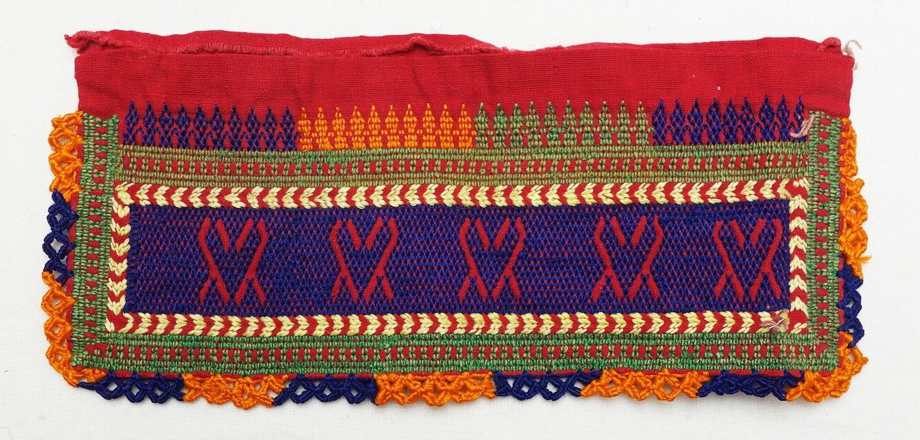 Sample of red cloth with an embroidered panel with a negative design set within a purple ground. Jordan, 20th century (TRC 2019.1715).