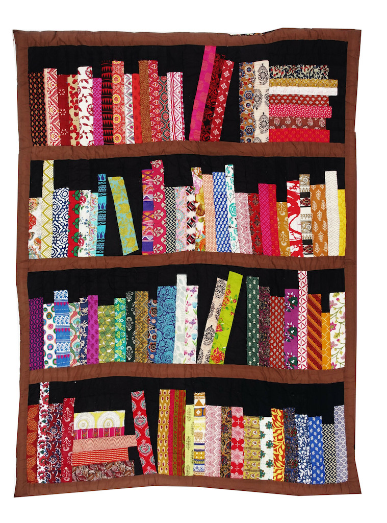 One of the most recent donations: An American, late 20th century quilt with a patchwork top decorated with a bookcase with four planks of books of different sizes made from a range of printed materials (TRC 2022.3129).