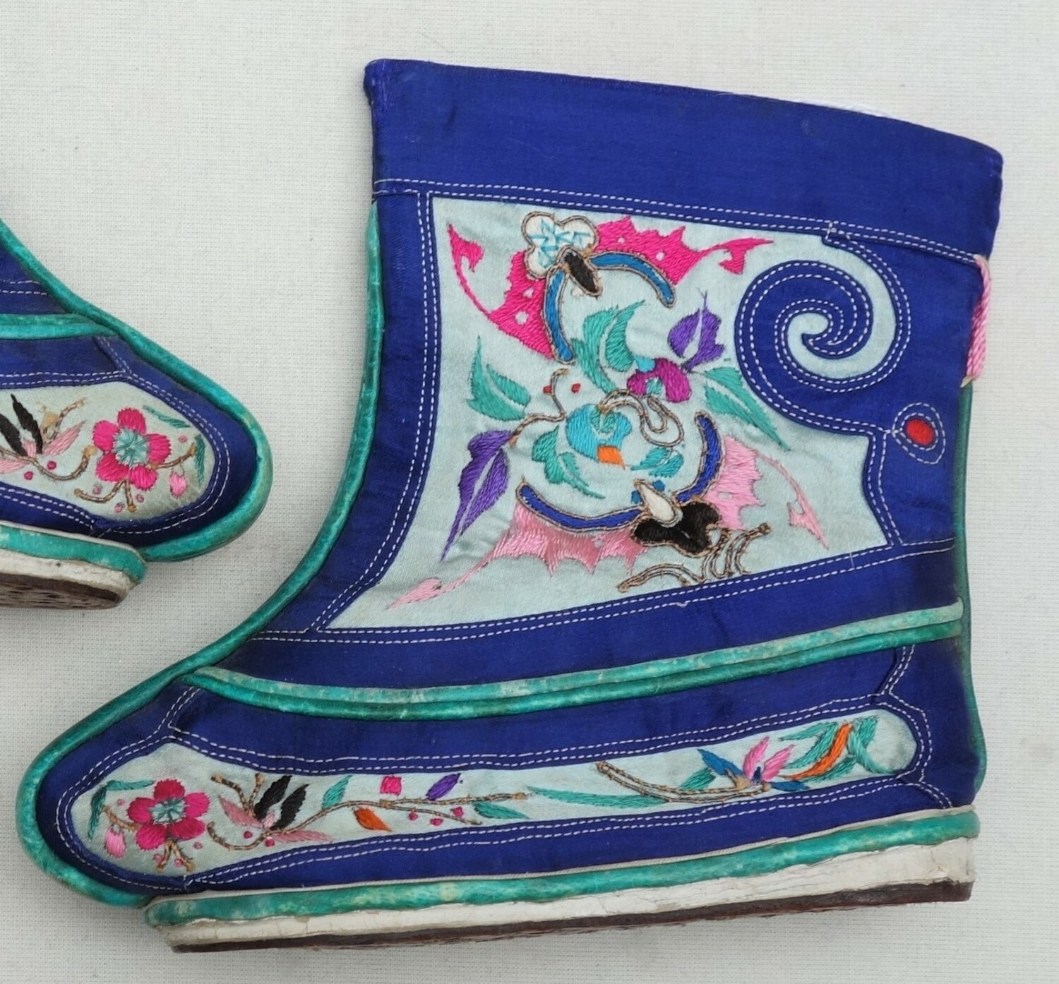Fig. 8. One of a pair of miniature ('lotus') boots in blue with green piping, as well as panels of embroidery with stylised bats, flowers and leaves in various colours. China, early 20th century (TRC 2023.1242a b).