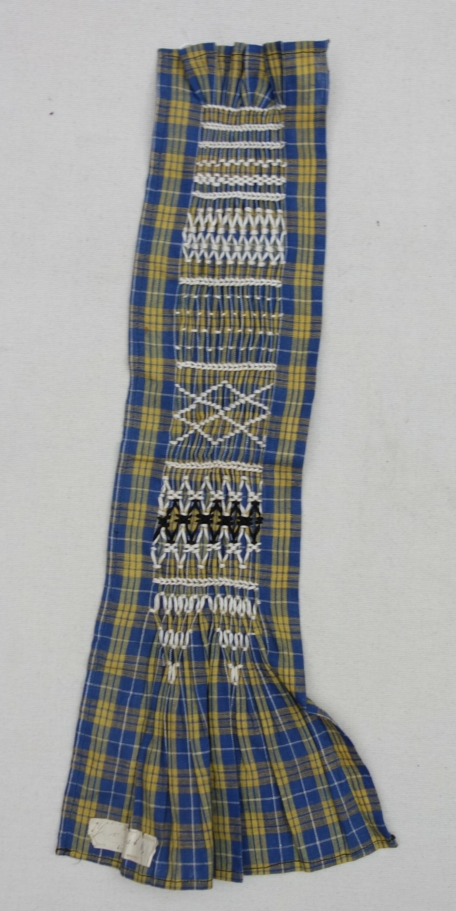 School sample of smocking using a blue and yellow checked cloth and red and black embroidery yarn. The Netherlands, 20th century (TRC 2023.1519).