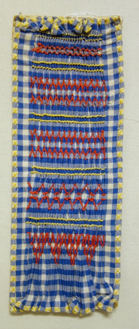 Sample of smocking using a blue and white gingham ground and embroidered with various smocking stitches using red and yellow yarns. The Netherlands, 20th century (TRC 2024.0160).