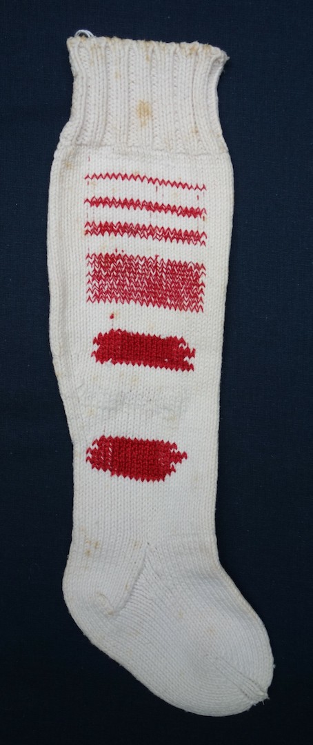 A complete hand knitted sock that has been mended in sixteen different manners using red and white yarn, the Netherlands, c. 1913-1915 (TRC 2024.0874.10).