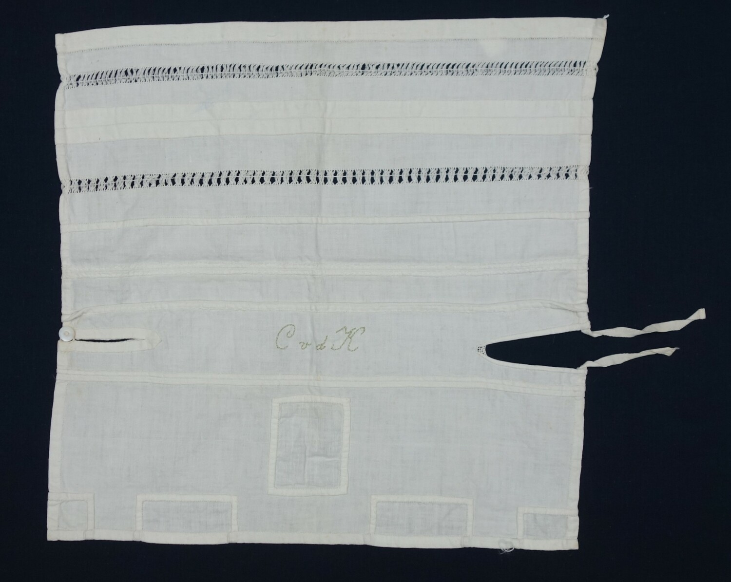 Fig. 7: Sample with a series of hems, seams, a neck opening with button, as well as patches, plus the initials  C vd K in green and white thread. Worked by Cato van der Kleij, Hoek van Holland, 1918 (TRC 2024.1725.03).