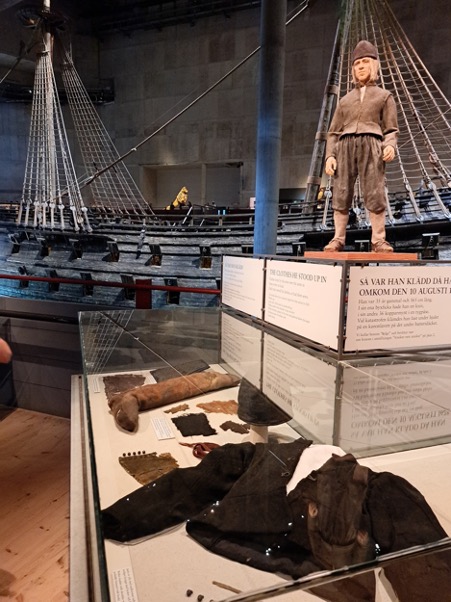 Fig 2: Showcases in front of the ship with preserved jackets, buttons (very similar in style to TRC 2024.2729 and TRC 2024.2618), brocaded fabric, shoes and mittens. Photograph by author.