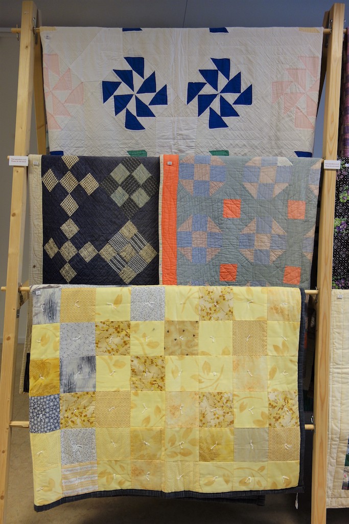 Display of quilts at the TRC Gallery exhibition 'Textile Tales from the Second World War'. The quilt on top is the twin of the missing quilt that was sent to Syria. The yellow quilt at the bottom of the rack was given to replace the missing quilt.