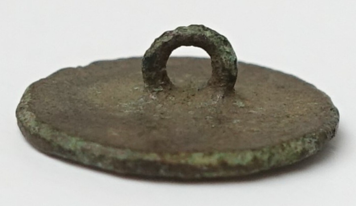Metal (pewter) button with a flat surface and an alpha-type shank. 18th century. TRC 2024.2595.